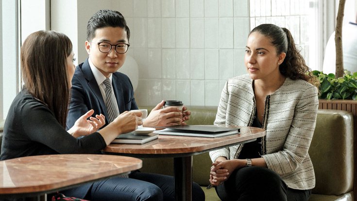 Photograph of three employees discussing at a coffee table